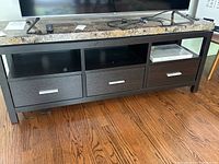 Front view of the TV stand showing marble top, two drawers, and open middle shelf with a TV and remote placed on top.
