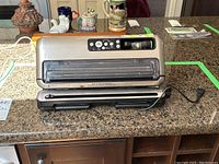 Front and side view of silver FoodSaver vacuum sealer showing design and layout on countertop.