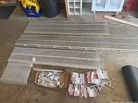 Full view of various white plastic coated wire shelves laid out on the floor with a box and plastic bags of mounting hardware