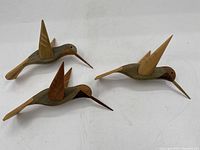 Three carved wooden hummingbirds shown together on a white surface, highlighting their shape and size.