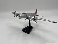 Photo showing front and left side of silver B-17 Flying Fortress model plane on black stand with red tail and wing tips.