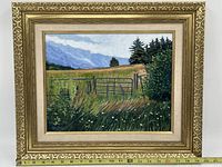 Full view of framed landscape painting showing grassy field, gate, trees, and mountains under a partly cloudy sky.