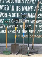 Full view of five garden tools upright against a backdrop, showing handles and heads for identification.