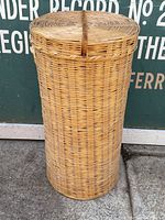 Photo of the larger nesting wicker basket with lid and leather strap displayed upright.