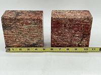 Two pink-red marble patterned stone bookends with a ruler for scale showing width around 4 inches each, front view.