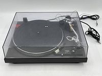 Front three-quarter view of turntable under clear dust cover showing platter, tonearm and control panel