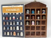 Wooden display case with 20 vintage and antique thimbles arranged in compartments alongside a 'Thimbles' reference book by Eleanor Johnson.