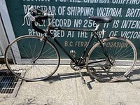 Side view of vintage black road bicycle showing full frame, drop handlebars with white wrap, and black leather saddle.