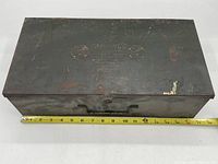 Closed rectangular metal carrying case of the Campingo camping stove with rust and worn surface.