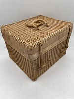 Side angle of rectangular woven wicker basket with hinged lid and sturdy handles.