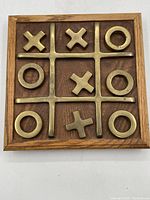 Top view of the brass and wood X and O game board with brass X and O pieces in place on wooden board with brass grid.
