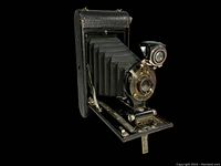 Front angled view of Kodak 1917 Model folding camera showing extended bellows, lens with gold-tone metal accents, folding base, and mounted viewfinder.