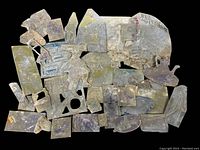 Overall view of 35 antique metal printing plates laid out showing varied sizes, shapes, and worn condition.
