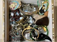Overview photo showing a variety of religious items and jewelry including crucifixes, rosary beads, bracelets, medallions, and chains inside a cigar box.