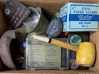 Overview of cigar box lot with corncob pipe, metal ashtray, paper clamps, and small collectibles