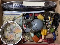 Overview of wooden cigar box filled with various items including a silver-tone mesh bracelet, pens, coins, and bead necklace.