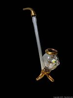 Full side view of the glass pipe showing tall clear stem, bent mouthpiece, round floral decorated bowl, and gold three-legged base.
