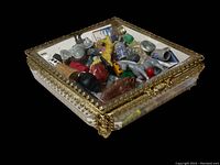 Glass case filled with assorted miniatures and game pieces set on a black background showing sides and top view.