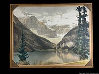 Front view of hand tinted antique Lake Louise photo showing mountain and lake scenery held by corner mounts on backing.