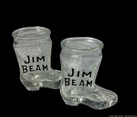 Pair of clear glass shot glasses shaped like cowboy boots with Jim Beam logo, showing front and side angles.
