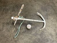 Large heavy antique metal anchor placed on floor beside a baseball for size reference.