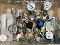 Top-down view of pressure gauges, valves and fittings in plastic bin