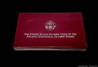Maroon presentation box with gold seal and inscription of the United States Olympic Coins of the Atlanta Centennial Olympic Games.