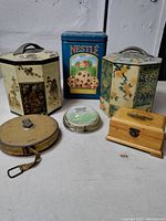 Photo of the lot showing all items including two oriental octagonal tins, Nestlé Tollhouse rectangular tin, Lufkin measuring tape, Grandfather Mountain paperweight, and small wooden box.