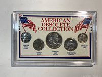 Top view of American Obsolete Collection display case showing five vintage U.S. coins mounted in card insert with two American flags and coin names.