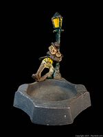 Front view of the antique cast iron ashtray featuring a figure leaning against a lamp post on a black background.
