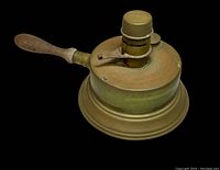 Side view of antique brass alcohol stove with wooden handle showing overall shape and condition.