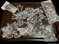 Top view of assorted clear glass lustres arranged on a brown textured tray, loose prisms and some in small plastic bags, various shapes including teardrops and octagonal beads.