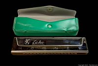 Image showing Hohner Echo harmonica with logo and green case open with button snap.