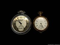 Pair of vintage pocket watches on black background showing front faces with details.
