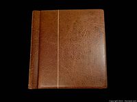 Brown leather-like stamp album displaying closed front cover with gold vertical line design.