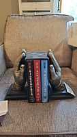 Pair of metallic finish hand sculpture bookends holding three hardcover Hunger Games books between them.