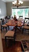 Dining room table with eight wooden cross-back chairs arranged around it, glassware on table.
