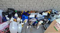 Photo showing large assortment of chemical containers including antifreeze, oils, and various auto chemicals arranged along a brick wall.