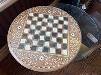 Top view of round inlaid Sisoo wood chess table with glass top showing chessboard squares and floral vine inlay