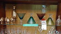 Wooden cabinet shelf containing the hand-painted decanter, matching six small glasses, three colored martini glasses, Wine 'O' glass and crystal bells