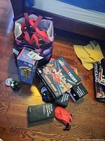 Photo showing a bag with pink straps, Tumbling Tower game box, two Cards Against Humanity boxes, a red ball pouch, and small marble-like toys scattered on floor.