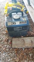 Blue TG 1200 ETQ generator with handle on top and visible dirt and leaves on ground under it.