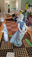 Photo of two porcelain figurines on a table; one girl holding a rabbit in blue dress and apron, other figurine nearby
