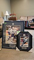 Two framed and glass-covered Toronto Maple Leafs hockey photo prints placed on carpet. Larger Wendel Clark print stands behind the smaller Doug Gilmour print.