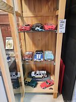 Shows three shelves inside glass cabinet with 15 vintage model cars in various colors and styles.