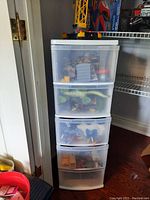 Front view of plastic organizer showing 5 drawers filled with assorted toys including trucks, cars, and animal figures.