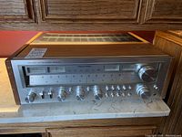 Front view showing aluminum face, dual meters, analog dial, and wood grain top and sides