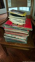 Stack of vintage vinyl records of various sizes and artists placed on wooden chair.