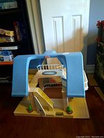 Front view of the Little Tikes toy house showing the blue peaked roof, front door, staircase, and base with bushes.