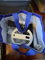 Blue and white tote bag with mostly Wii game cases and white Wii wheel attachments visible inside.